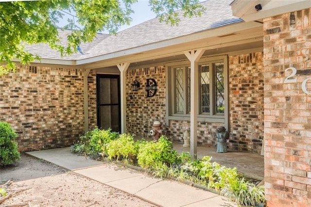 entrance to property featuring covered porch, brick siding, and a shingled roof