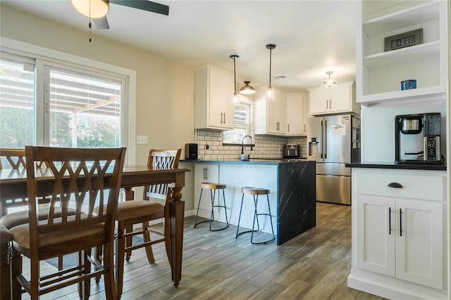 kitchen with a peninsula, wood finished floors, dark countertops, high end fridge, and backsplash