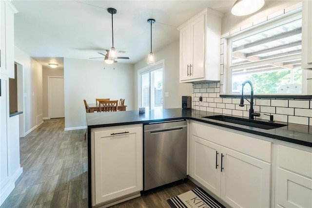 kitchen featuring stainless steel dishwasher, a peninsula, dark countertops, tasteful backsplash, and a sink
