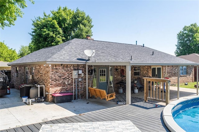 back of house with brick siding, a shingled roof, a wooden deck, and a patio