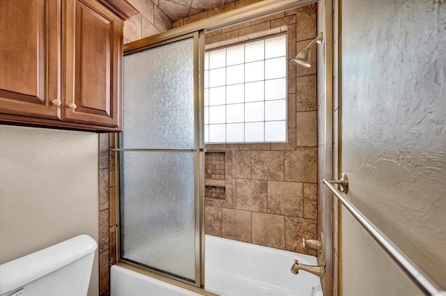 full bathroom with bath / shower combo with glass door, toilet, and a wealth of natural light