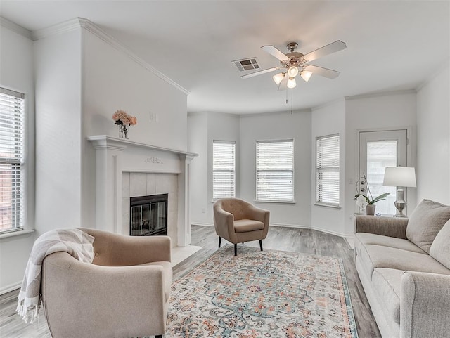 living area with a tiled fireplace, visible vents, baseboards, ceiling fan, and light wood-style floors