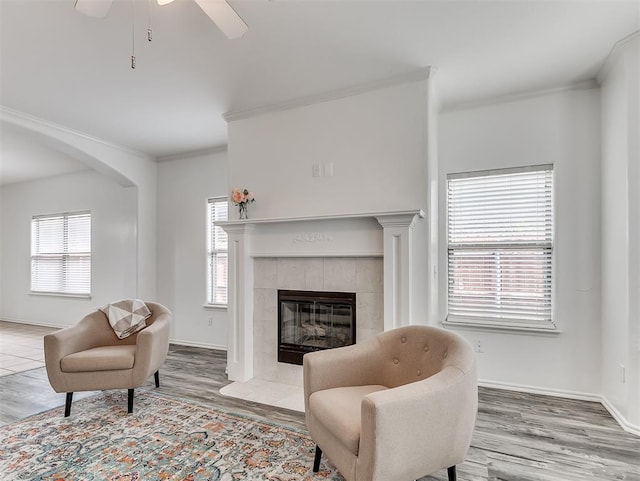 living room featuring baseboards, ceiling fan, a tiled fireplace, and crown molding