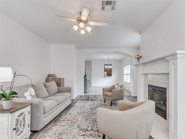 living room featuring ornamental molding, visible vents, ceiling fan with notable chandelier, arched walkways, and a fireplace