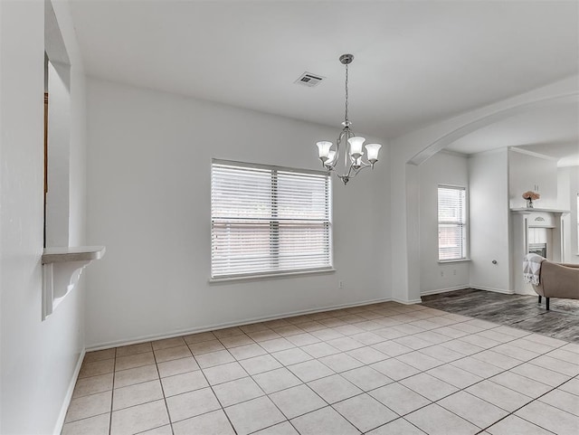 unfurnished dining area featuring arched walkways, an inviting chandelier, visible vents, and light tile patterned flooring