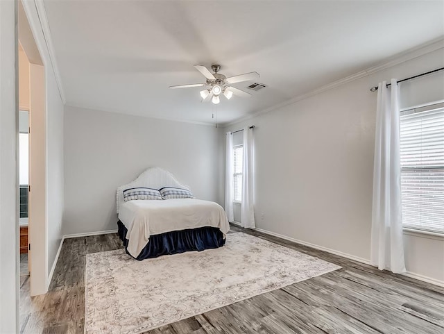 bedroom with baseboards, ornamental molding, visible vents, ceiling fan, and wood finished floors