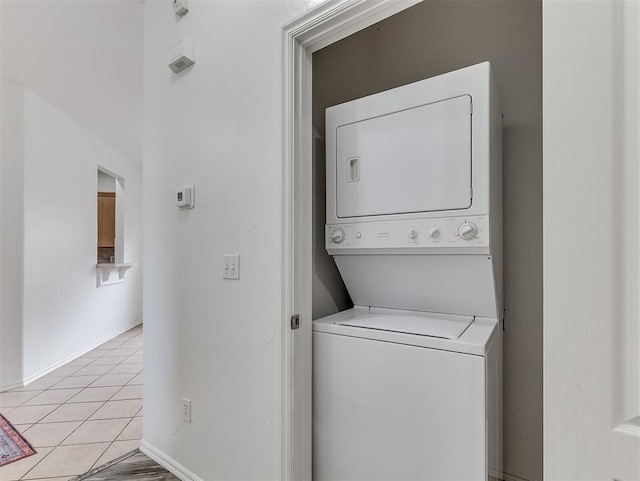 washroom featuring laundry area, light tile patterned flooring, stacked washer / drying machine, and baseboards