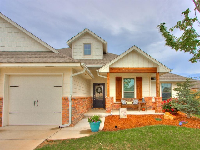 craftsman inspired home with covered porch, roof with shingles, a garage, concrete driveway, and brick siding