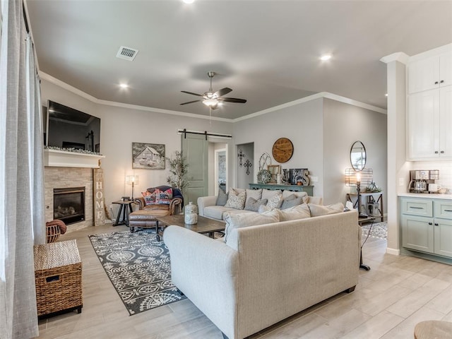 living area featuring a ceiling fan, crown molding, a barn door, a glass covered fireplace, and light wood finished floors