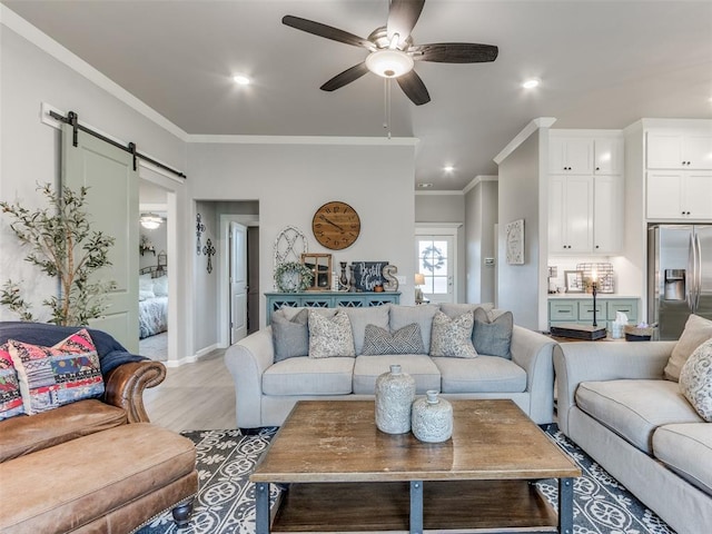 living area with a barn door, a ceiling fan, recessed lighting, ornamental molding, and light wood-style flooring