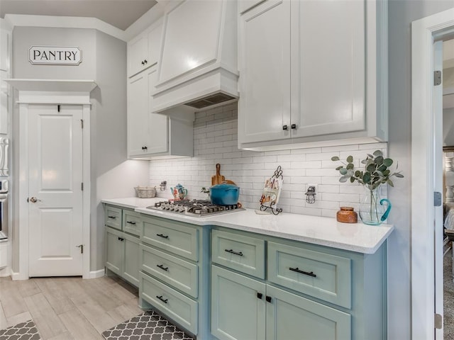 kitchen featuring custom range hood, appliances with stainless steel finishes, tasteful backsplash, light wood-type flooring, and green cabinets