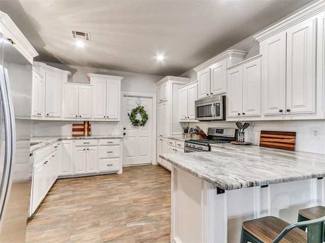 kitchen featuring a peninsula, white cabinetry, visible vents, backsplash, and appliances with stainless steel finishes