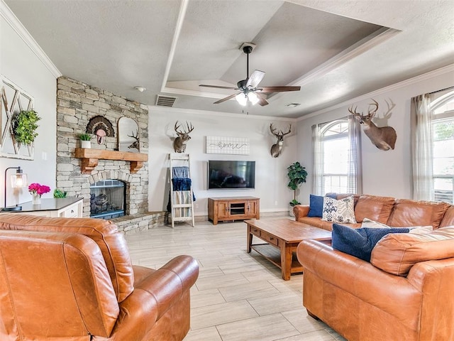 living room with a tray ceiling, visible vents, ceiling fan, crown molding, and a fireplace