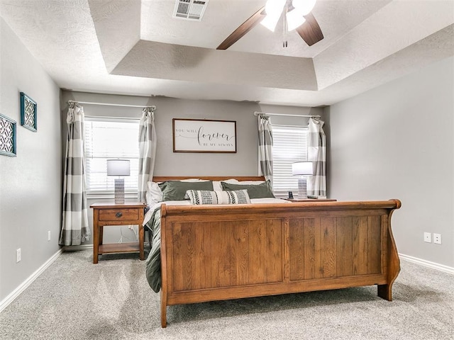 bedroom with multiple windows, light carpet, and a raised ceiling