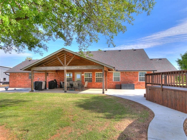 rear view of property with a lawn, a patio area, roof with shingles, and brick siding