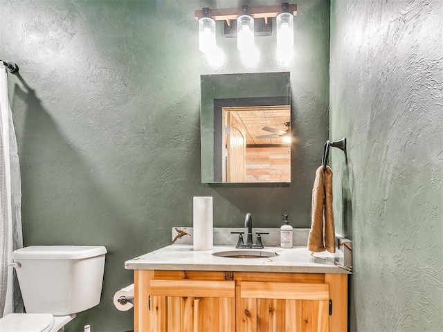 bathroom with vanity, toilet, and a textured wall