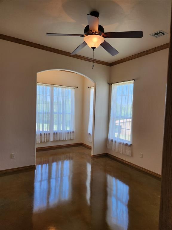 spare room featuring baseboards, plenty of natural light, finished concrete flooring, a ceiling fan, and crown molding