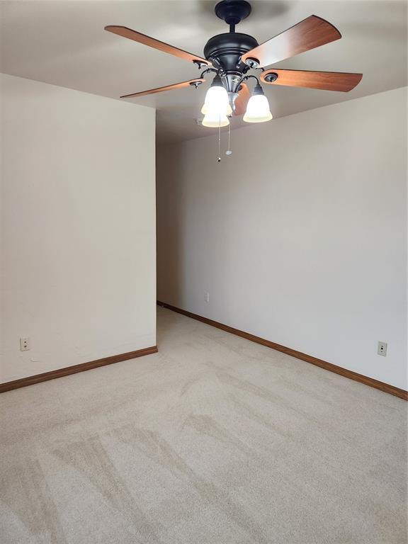 empty room featuring ceiling fan, light colored carpet, and baseboards