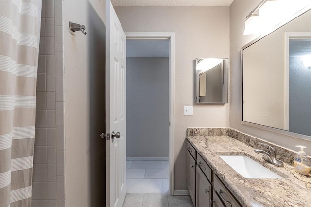 full bath with vanity, baseboards, tile patterned floors, and tiled shower