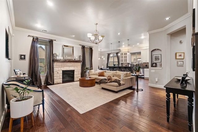living area with an inviting chandelier, dark wood-type flooring, a stone fireplace, and crown molding