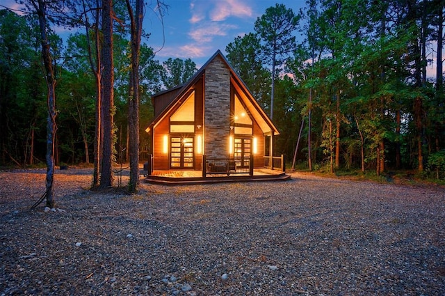 back of house at dusk with french doors and stone siding