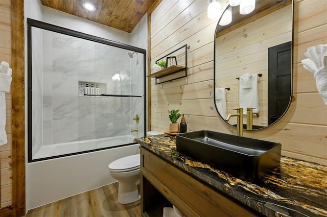 bathroom with wood finished floors, wooden walls, enclosed tub / shower combo, toilet, and vanity