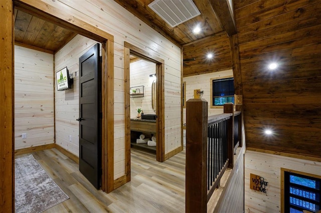 corridor with wooden ceiling, wooden walls, wood finished floors, and an upstairs landing