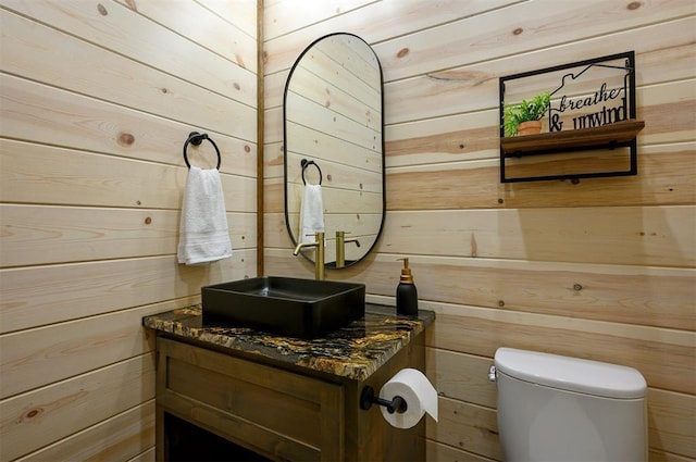 bathroom with wooden walls, toilet, and vanity