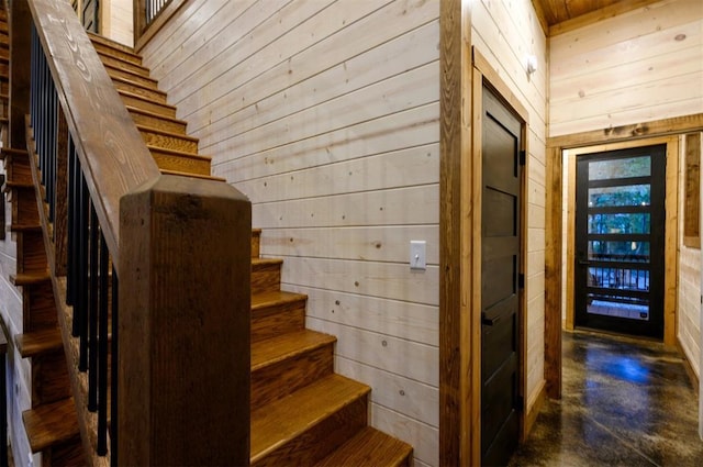 staircase featuring wood walls and finished concrete floors