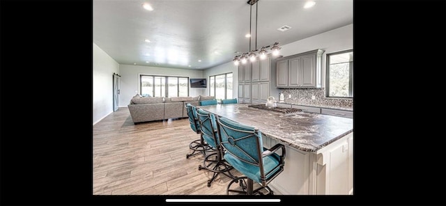 kitchen featuring gray cabinets, a breakfast bar, light wood-type flooring, a kitchen island with sink, and backsplash
