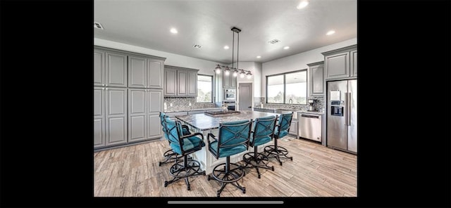 kitchen with a breakfast bar area, backsplash, a center island, gray cabinetry, and appliances with stainless steel finishes