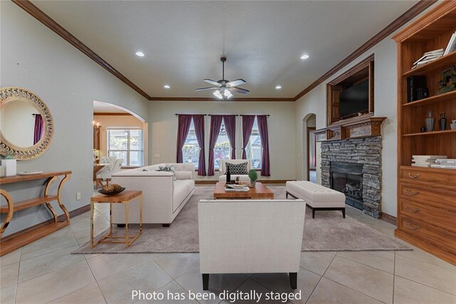 living area featuring crown molding, a fireplace, a ceiling fan, and arched walkways