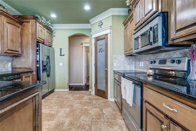 kitchen featuring appliances with stainless steel finishes, crown molding, arched walkways, baseboards, and dark stone counters
