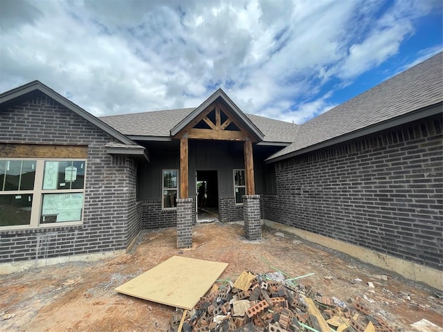 entrance to property featuring brick siding and roof with shingles
