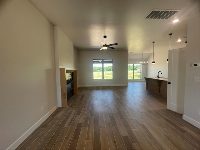 5012 Misty Wood Ln, Mustang, OK 73064 - unfurnished living room with dark wood finished floors, a ceiling fan, a glass covered fireplace, and a chandelier