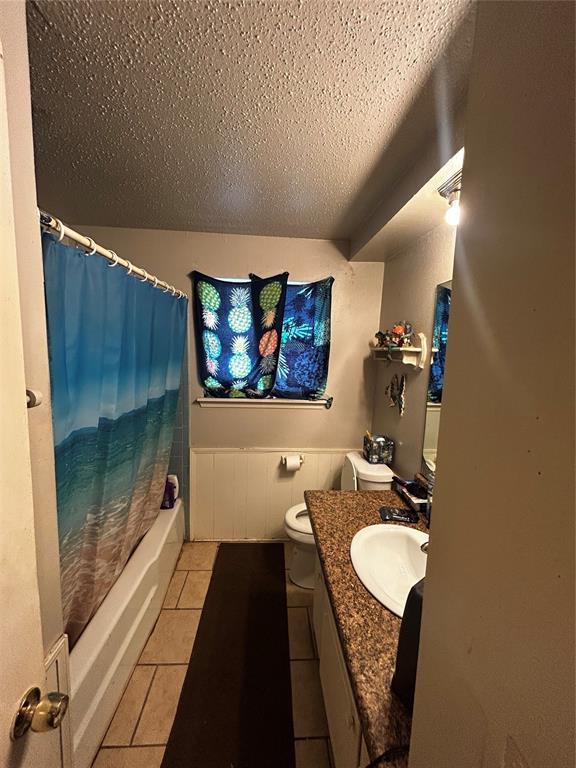 full bath featuring toilet, shower / bath combo, tile patterned floors, a textured ceiling, and vanity