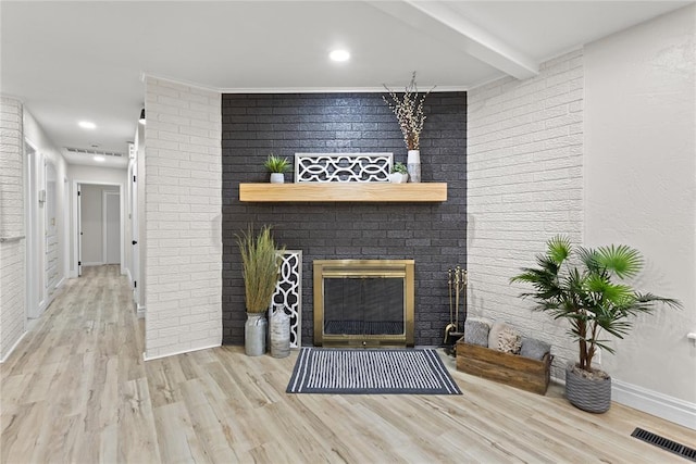 living room featuring baseboards, brick wall, visible vents, wood finished floors, and a fireplace
