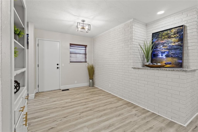 interior space with brick wall, light wood finished floors, baseboards, and visible vents
