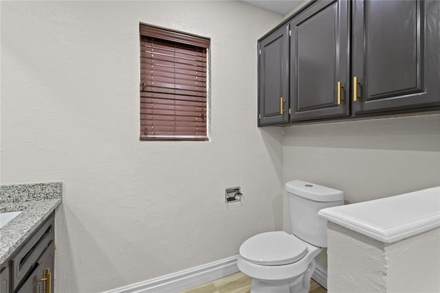 half bath with toilet, baseboards, vanity, and wood finished floors