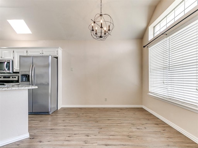 kitchen with stainless steel appliances, a chandelier, lofted ceiling, light wood-style floors, and white cabinets