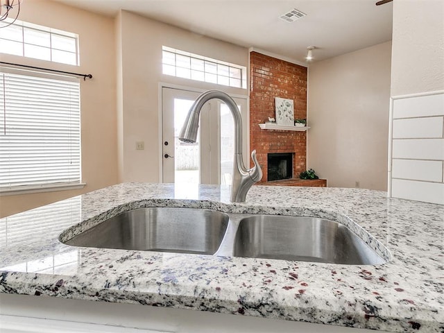 kitchen view of a sink, light stone counters, and a fireplace
