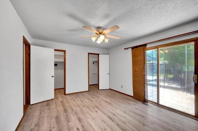 unfurnished bedroom with light wood-style flooring, a textured ceiling, visible vents, access to outside, and a spacious closet