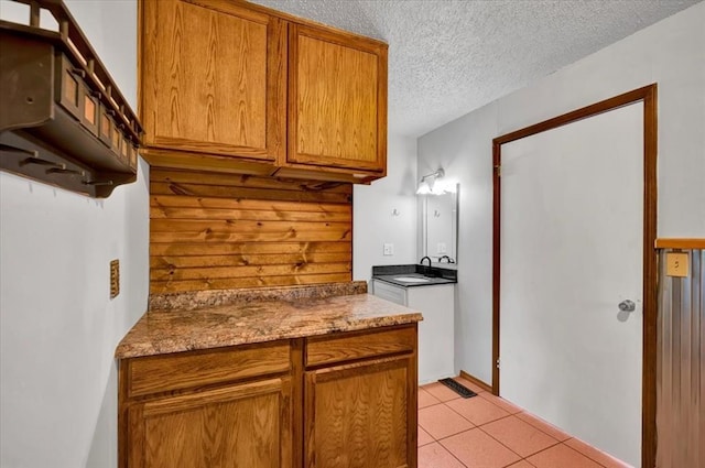 kitchen featuring brown cabinetry, a sink, light tile patterned flooring, and a textured ceiling