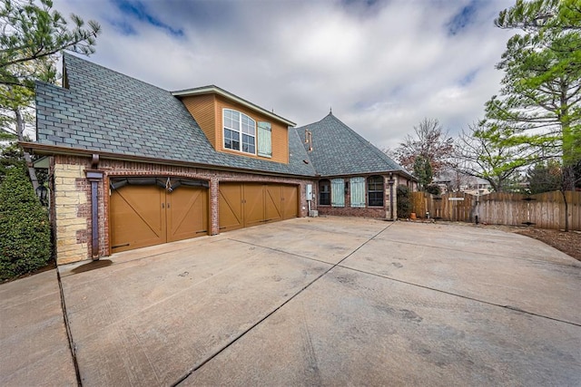 view of home's exterior with driveway, brick siding, fence, a garage, and a high end roof