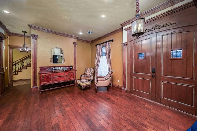 foyer featuring an inviting chandelier, dark wood finished floors, visible vents, ornamental molding, and stairs
