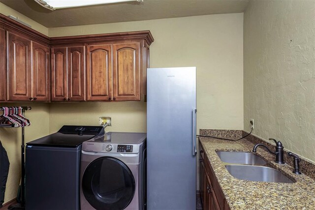 laundry room featuring cabinet space, a textured wall, washer and clothes dryer, and a sink