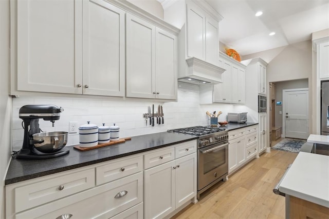 kitchen featuring stainless steel appliances, light wood-style floors, backsplash, white cabinetry, and vaulted ceiling