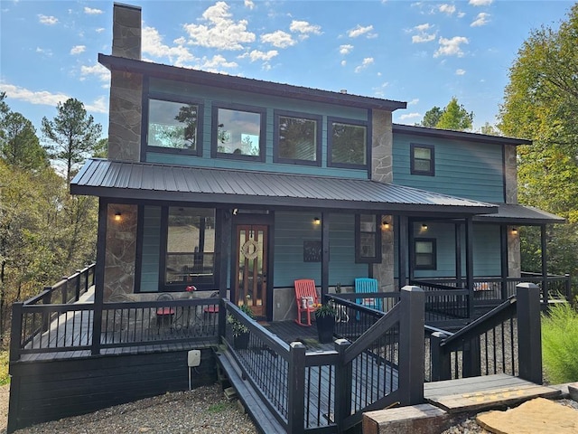 rear view of property featuring a chimney, metal roof, covered porch, and stone siding