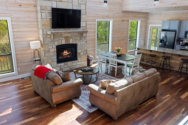 living room featuring a fireplace, dark wood-style flooring, wooden walls, and visible vents