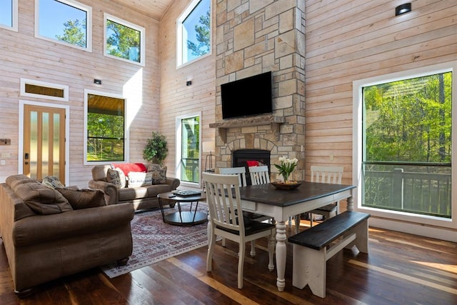 dining area with wood walls, a stone fireplace, wood-type flooring, and high vaulted ceiling